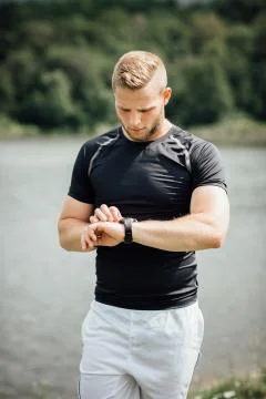 Runner standing at a pond checking time on his watch Stock Photos
