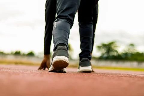 Runner at starting line, focused on athletic shoes on track, preparing for ra Stock Photos