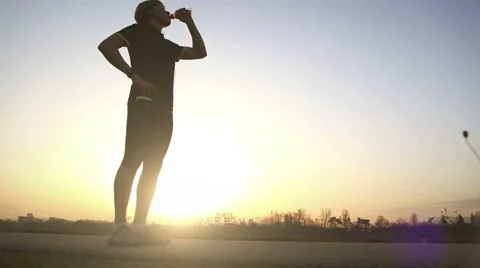 A runner stops after a scamper to have a sip of water and proceeds walking Stock-Footage 56411784