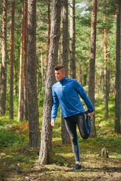 Runner stretching leg at tree in woods Stock Photos