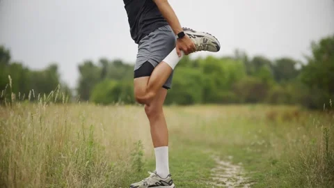 Runner stretching quadriceps before marathon training on grassy field Stock Footage 313951541