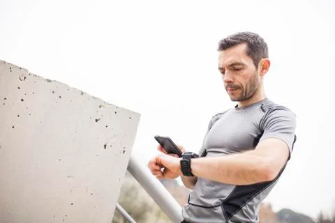 Runner synchronizing his watch and smart phone Stock Photos