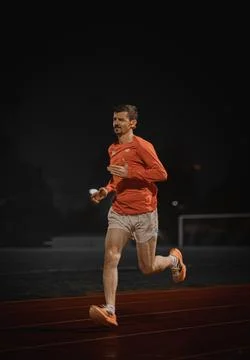 Runner turned towards the camera on a red athletics track at night Stock Photos