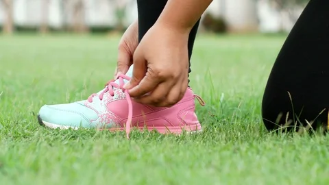 Runner is tying up her shoelaces on the grass.Prepare Before Exercise Stock Footage 98416728