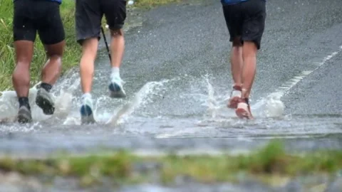 Runners are training in the rain passing through a waterlogged road Video stock 307435028