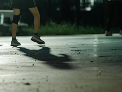 Runner's Legs Casting Long Shadow on Pavement During Night Exercise Stock Photos