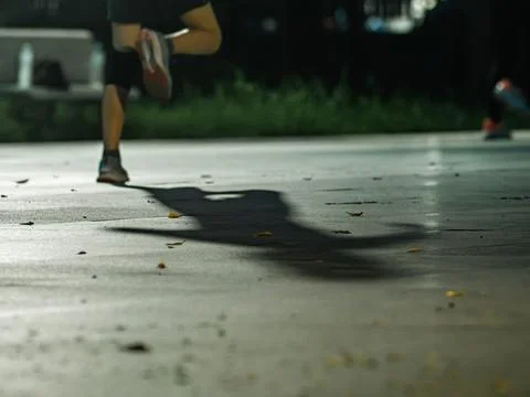 Runner's Legs Casting Long Shadow on Pavement During Night Exercise Stock Photos