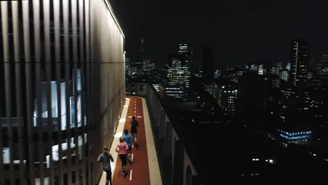 Runners on rooftop running track at night with London skyline, drone aerial 4K Stock Footage 101169521