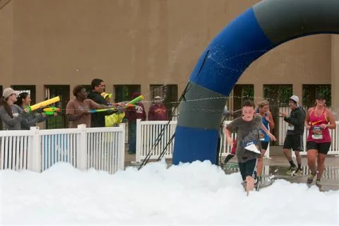Runners run through squirt guns and foam at 5k race Stock Photos