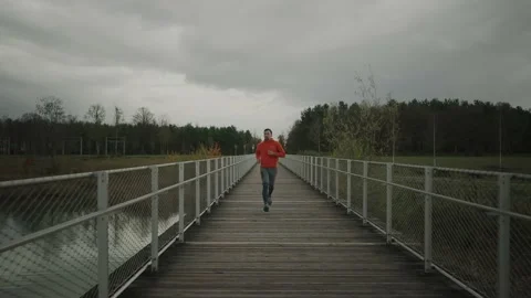 Running in cold fall weather in nature. A man runs across wooden bridge in Stock Footage 221567543