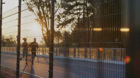 Running couple seen through an athletic field fence Stock Footage 100033405