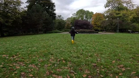 Running on the Grass Boy in Yellow Rubber Boots, Hat, and Jacket Stock Footage 254079521