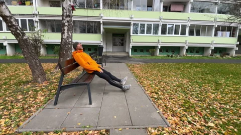 Running man in orange waterproof jacket resting on the bench. Runner is dressed Stock Footage 324515055