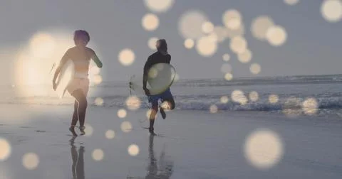 Running pair carrying leashed boards along wet sand at beach low tide, in Fotos Stock