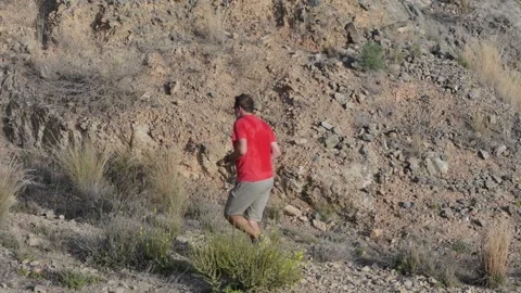 Running on a rocky trail, a man in a red shirt and shorts trains in the mor.. Video stock 285022047