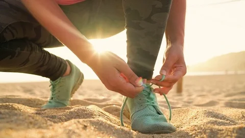Running shoes - woman tying shoe laces on sandy beach at sunset. Slow motion Stock Footage