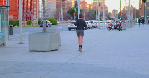 Running into the Sunset with a Cityscape Backdrop Stock Footage 298035158