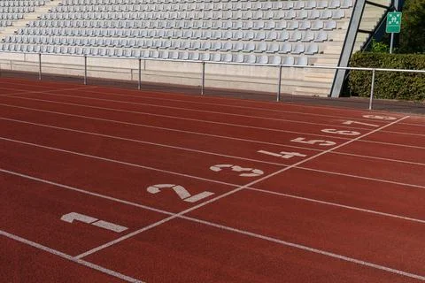 Running track with numbered lanes in an empty stadium during daylight Stock Photos