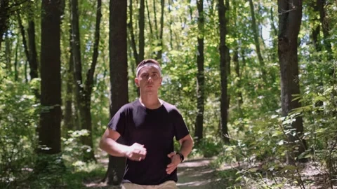 Running training program in a forest setting. A man runs in the park, smiles at Stock Footage 280186340