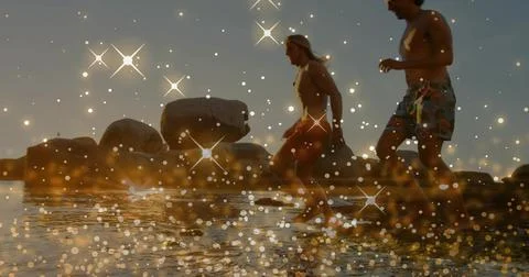 Running two men in trunks splashing in shallow water at shoreline, boulders, Stock Photos