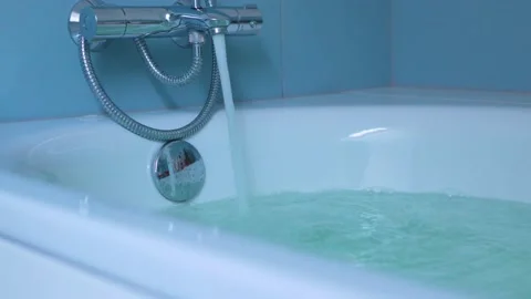 Running water pouring from faucet tap filling white bath tub in blue bathroom Stock Footage