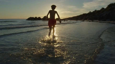 Running in water waves of ocean beach, a little boy at sunset Video stock 234977856