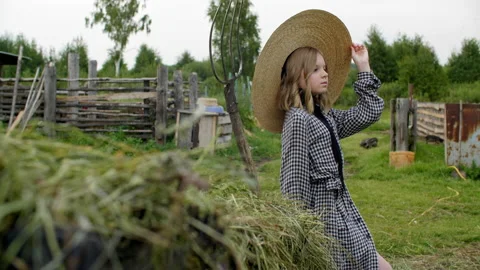 Rural girl in hat posing on haystack and hayfork background in countryside Stock Footage 140480447