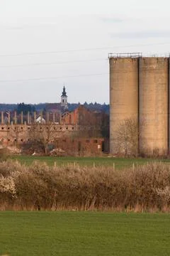 Rural Landscape Featuring Farm Structures, Distant Church Tower, and Green .. Stock Photos