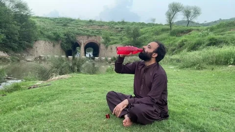 Rural Pakistani Man Drinking Water While Relaxing in Scenic Landscape Stock Footage 344759792