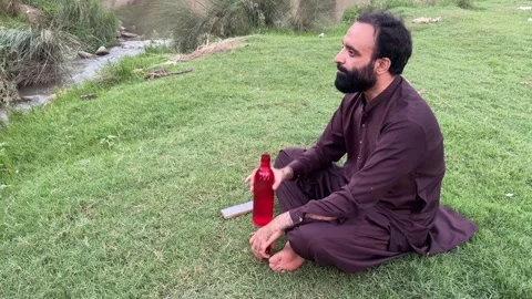 Rural Pakistani Man Drinking Water and Relaxing Beside Natural Stream Stock Footage 344760729