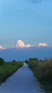 Rural path through green fields under a blue sky with clouds Stock Photos