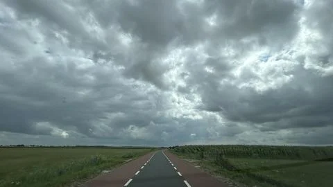Rural road stretching through flat green fields beneath dramatic storm clouds Stock Photos