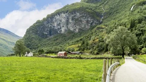 Rural road through green fields and traditional houses in Norwegian valley Stock Photos