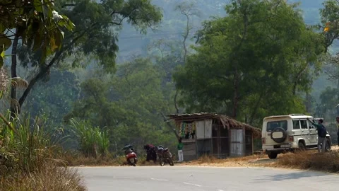 Rural roadside tea stall with parked SUV and motorcycles in forested hill area Stock Footage 328825009