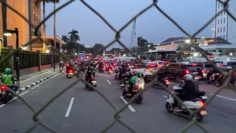 Rush hour traffic seen through a chain-link fence shows dense streams of cars Видео 333807951