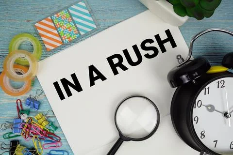 In A Rush text on a paper surrounded by office supplies, a magnifying glass.. Stock Photos