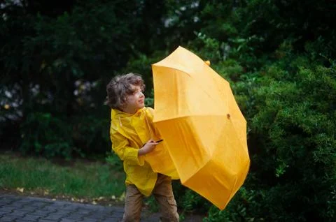 Rushes of heavy wind force down from the boy&amp;#39;s legs with a yellow umbrell Stock Photos
