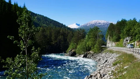 A rushing mountain stream and a paved highway with cars in the mountains. Stock Footage 116489272