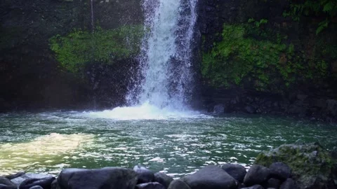 A rushing natural waterfall surrounded by cliffs and lush green trees Vídeos de archivo 339039562