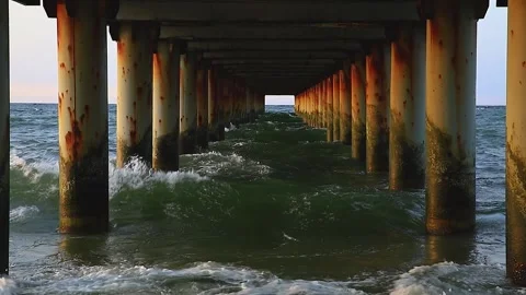 Rushing sea under the pier columns in the evening at sunset, slow motion. Stock Footage 143960355
