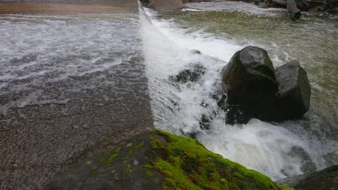A rushing stream flows over a small concrete spillway Stock Footage 336985446