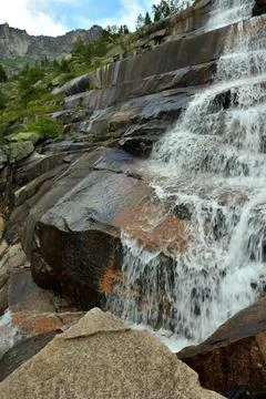 A rushing stream flows in a rapid cascade from high stone steps on a sunny .. Stock Photos