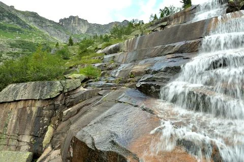 A rushing stream of water flows down the stone steps of a natural waterfall.. Stock Photos