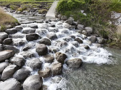 Rushing water flows over smooth gray stones. White foam dances as stream tumbles Stock Photos