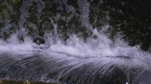 Rushing water stream creating foam and bubbles over a small cascade in a natural Stock Footage 346171494