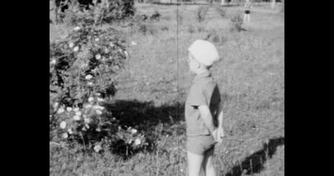 Russia - circa 1970s: Soviet boy in white hat looking at flower bush in garden Vidéo 328361813