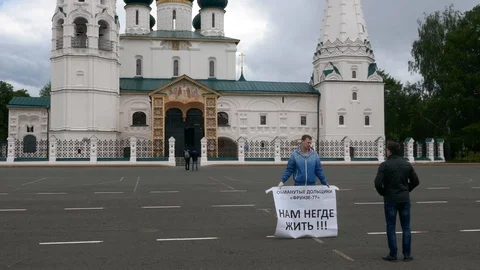 Russian activist with a banner standing in square near an orthodox church Stock Footage 99256455