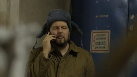 Russian hacker in the hat with earflaps speaks on the phone in the basement. A Stock Footage 107326631