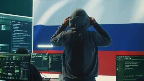 Russian hacker with a hood installing panic by misconception and manipulation Stock Photos