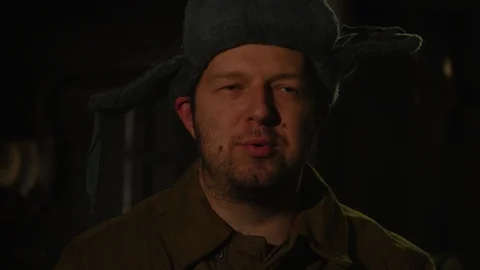 Russian man in a hat with earflaps, talking on the phone in a dark basement and Video stock 107324230